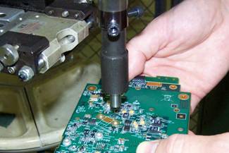 Photo of a PC Board in manufacturing process with broach fasteners being applied to the board.